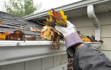 Gloved hand clearing leaves from gutters