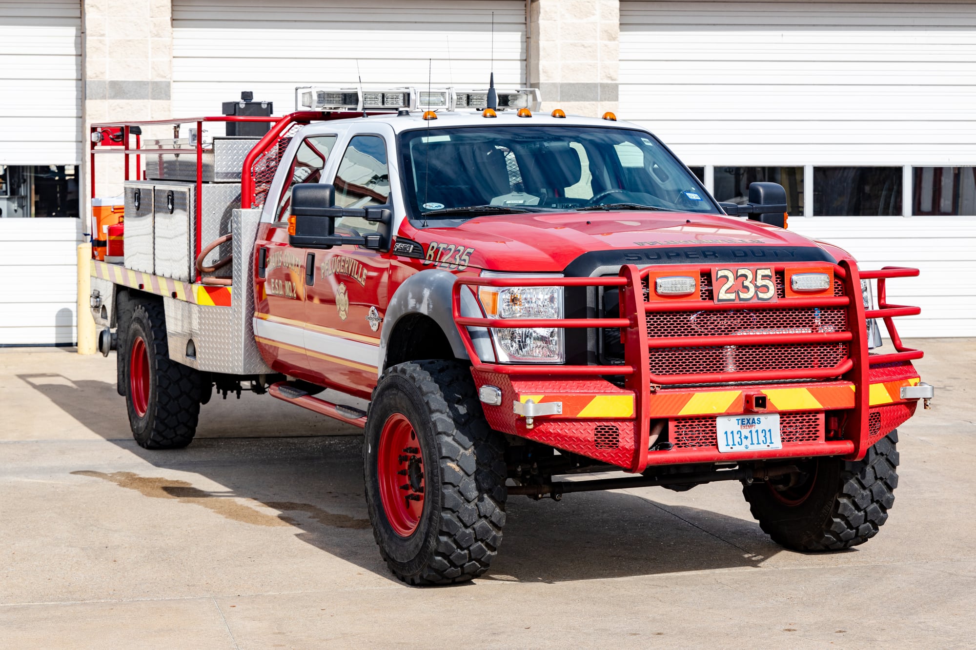 Red Pflugerville Fire Department Brush 235 wildland truck parked outside the station bay.