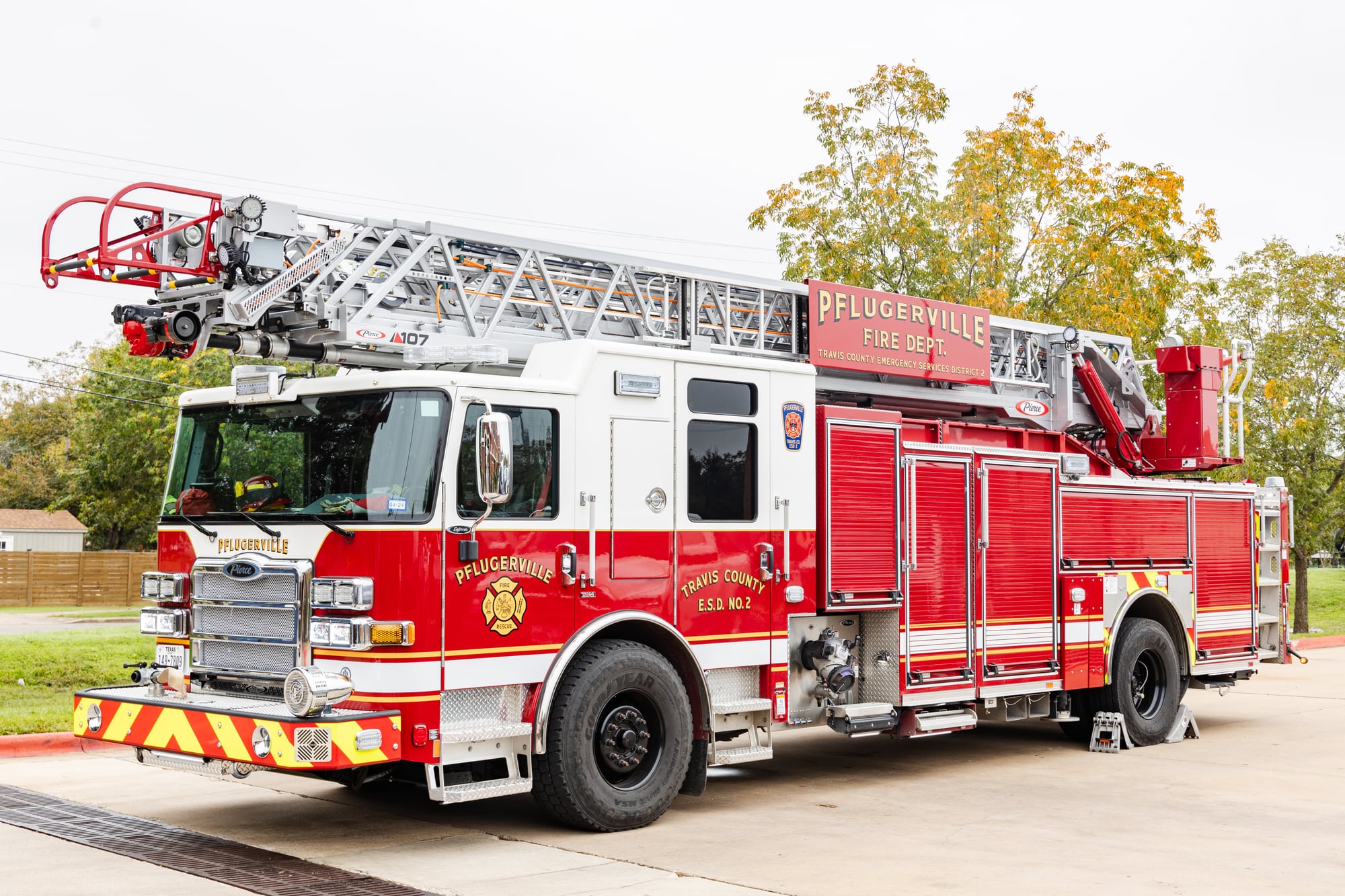 Red and white Pflugerville Fire Department Quint 211 aerial ladder truck parked outdoors.