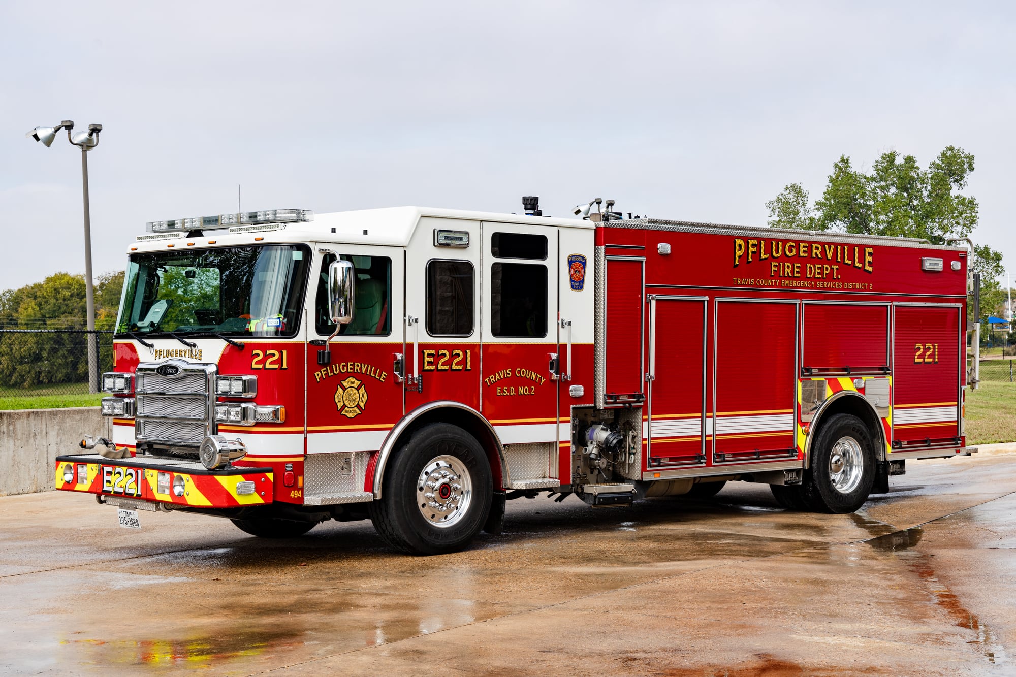 Red and white Pflugerville Fire Department Engine 221 pumper parked on wet pavement.