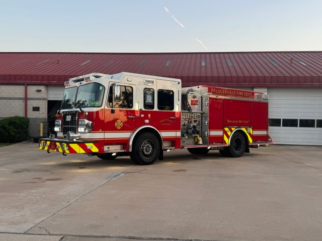 Red and white Pflugerville Fire Department Engine 241 pumper parked in front of station doors.