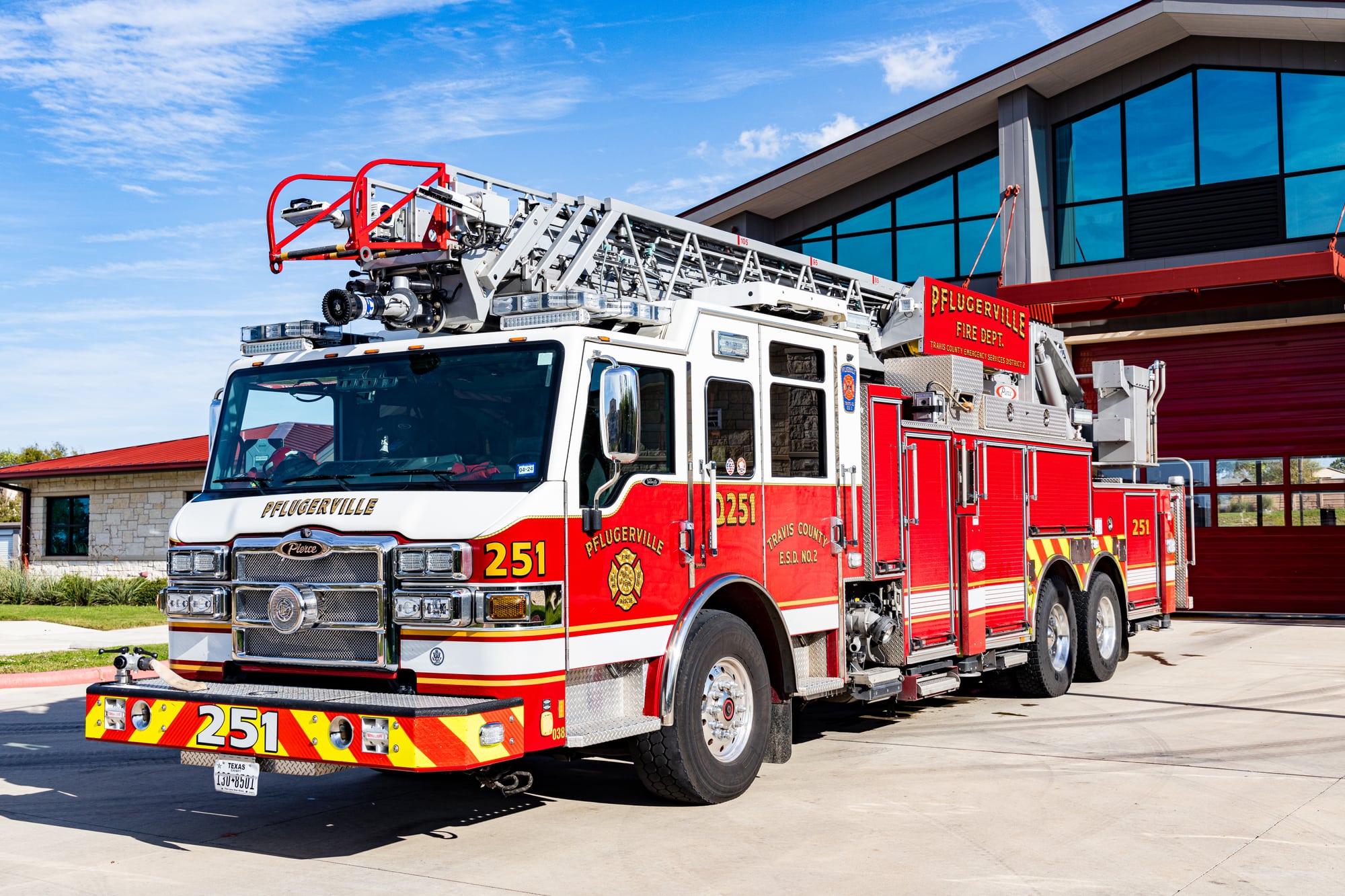 Red and white Pflugerville Fire Department Quint 251 aerial ladder truck parked at the station.
