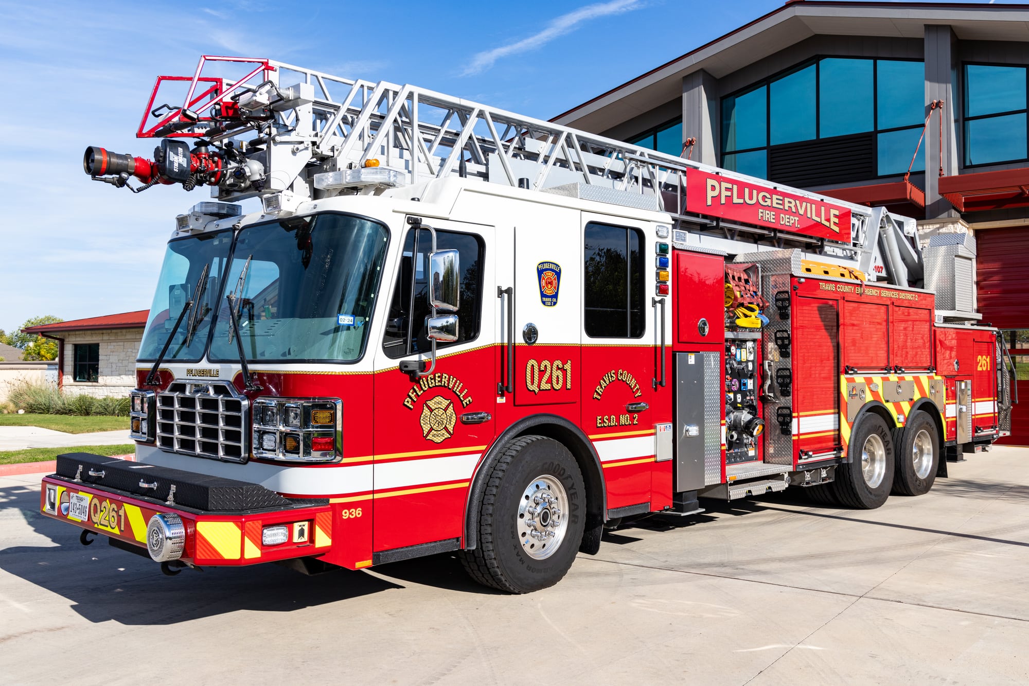 Red and white Pflugerville Fire Department Reserve Quint 202 aerial ladder truck parked outside the station.