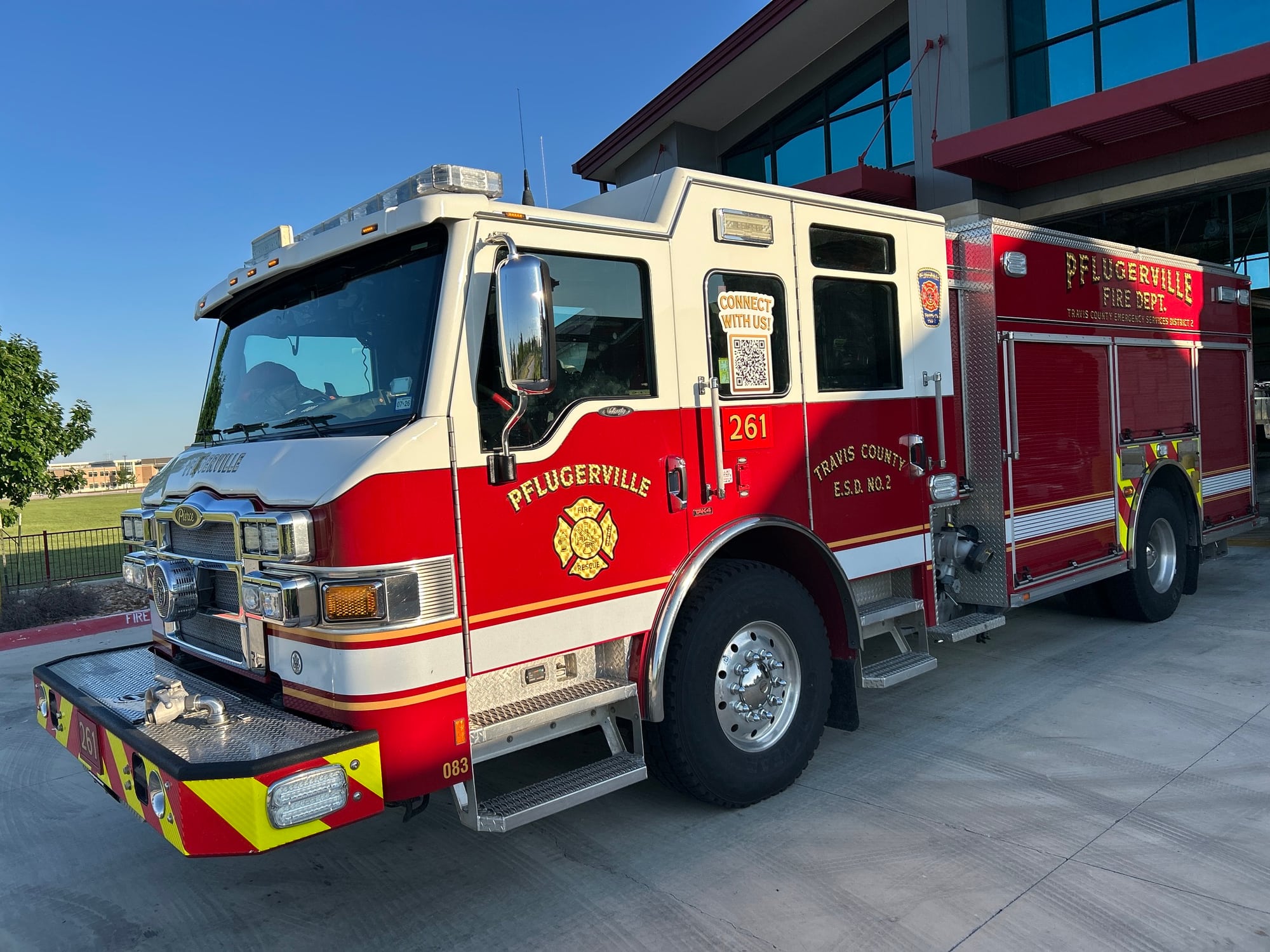 Red and white Pflugerville Fire Department Engine 261 pumper parked beside a station building.