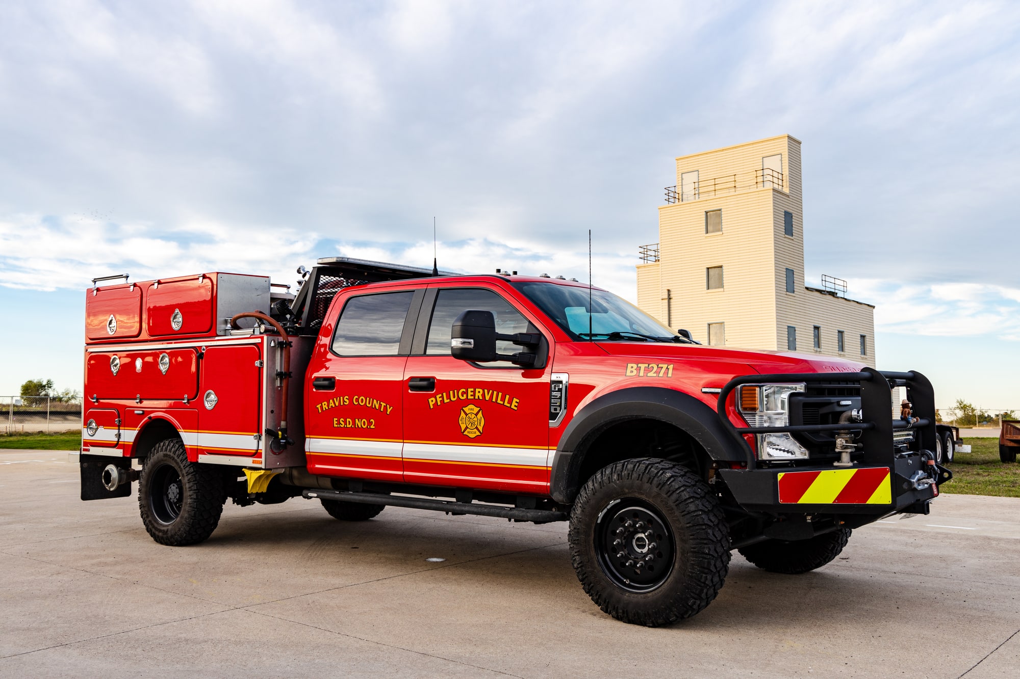 Red Pflugerville Fire Department Brush 271 wildland truck parked outdoors near a training tower.