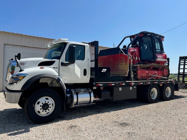 White haul truck carrying a red Pflugerville Fire Department bulldozer on a flatbed trailer.