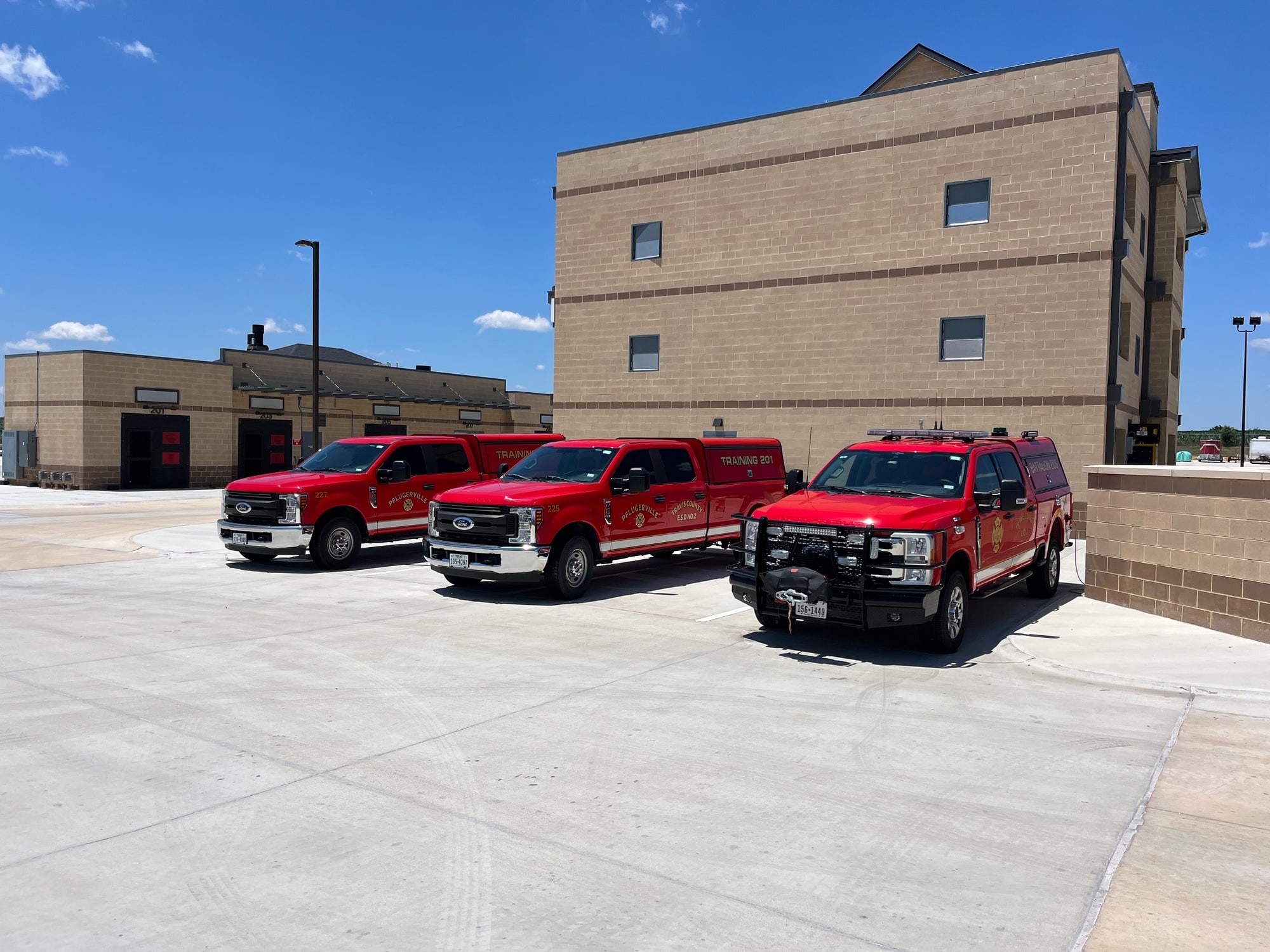 Three red Pflugerville Fire Department training vehicles parked in front of a training tower.